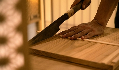 Person cutting wood with traditional tool on a wooden table, showcasing craftsmanship and precision in woodworking.