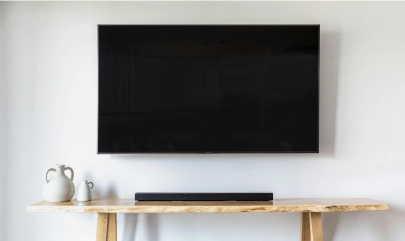 Wall-mounted TV above a wooden console with pottery decor and soundbar. Modern living room setup.