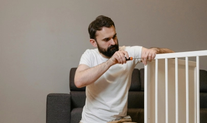 Man assembling baby crib with screwdriver in living room.