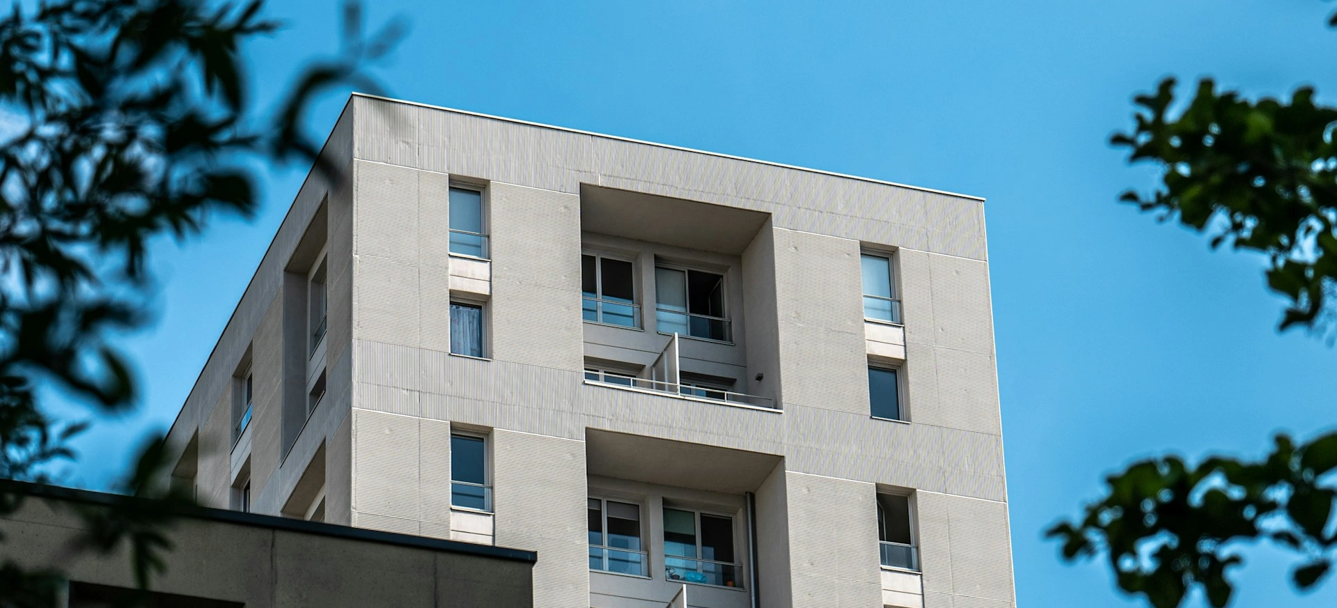 Modern apartment building under clear blue sky, surrounded by trees.