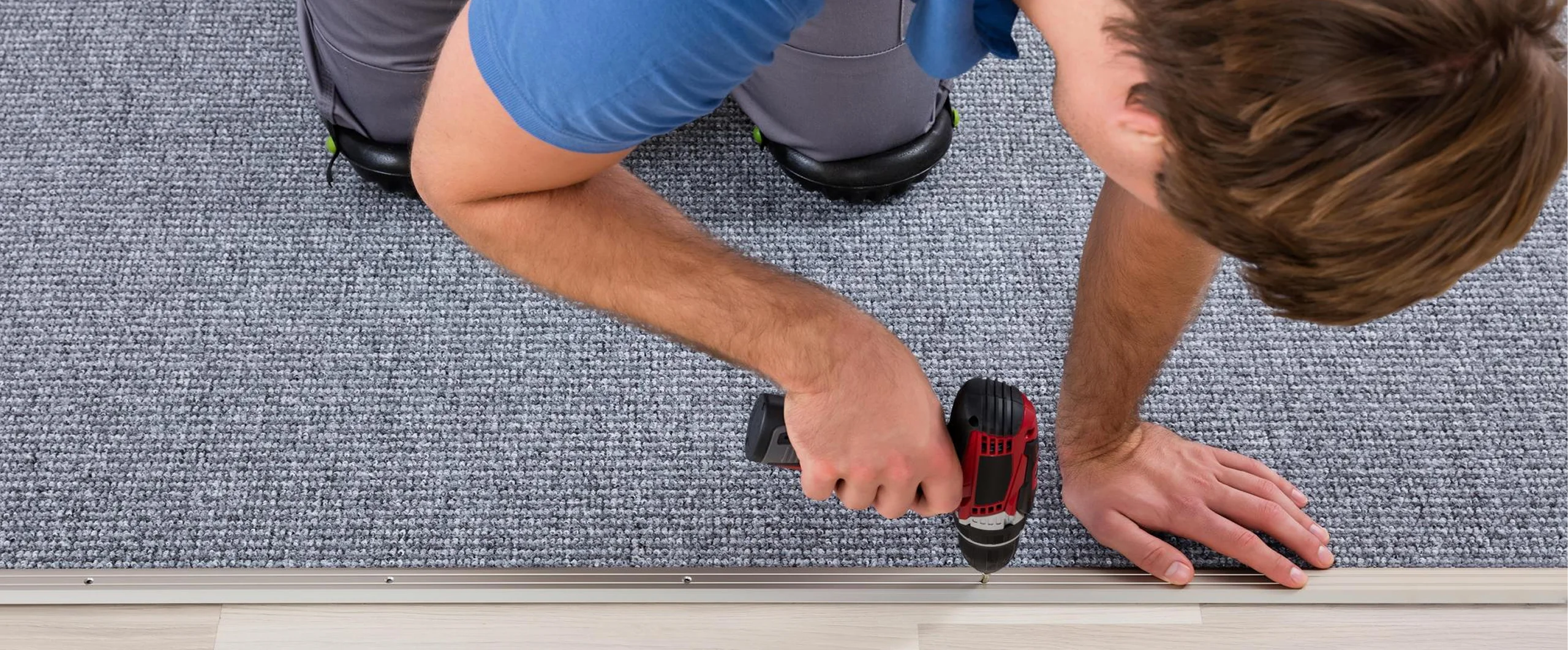 Technician securing carpet edging with a power drill.